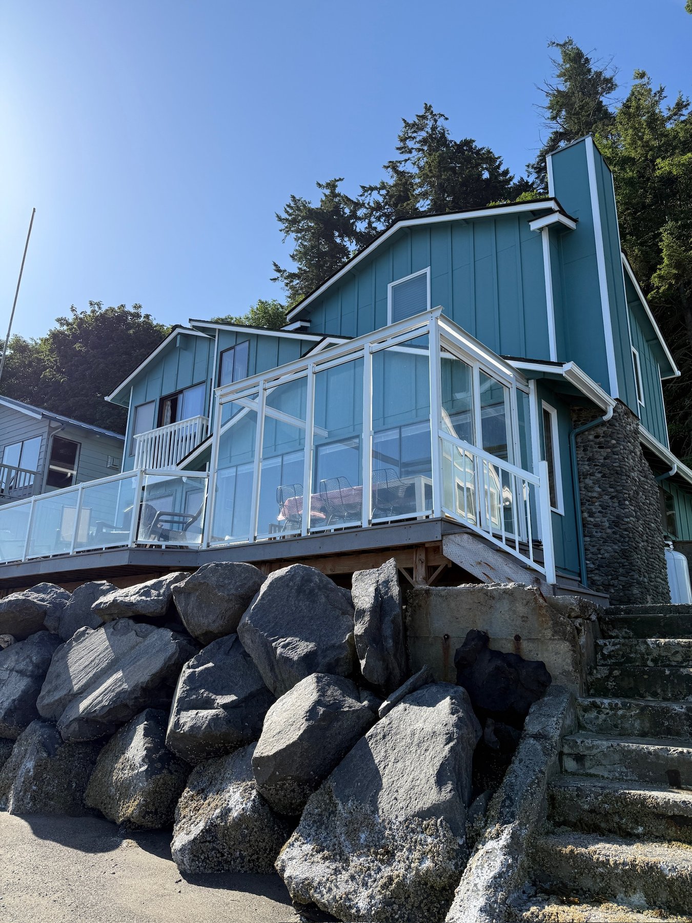 Exterior of Whidbey Seaside Cottage showing teal siding, stone base, and beachfront location