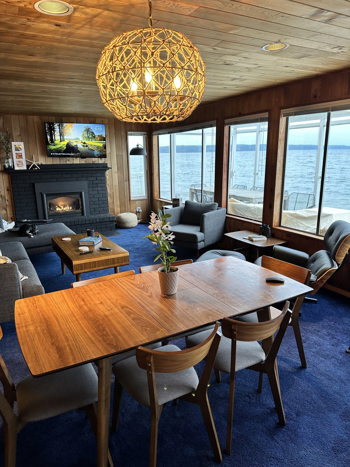 Open-plan living and dining room with chandelier, fireplace, and panoramic water views